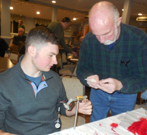 Fred Lord judges an entry from Tristan Wilgan (seated), winner of last year's Chopped fly tying contest at the Nutmeg TU Holiday Party. This year's contest will be held Tuesday, Dec. 19, at 7 p.m. at Port 5.
